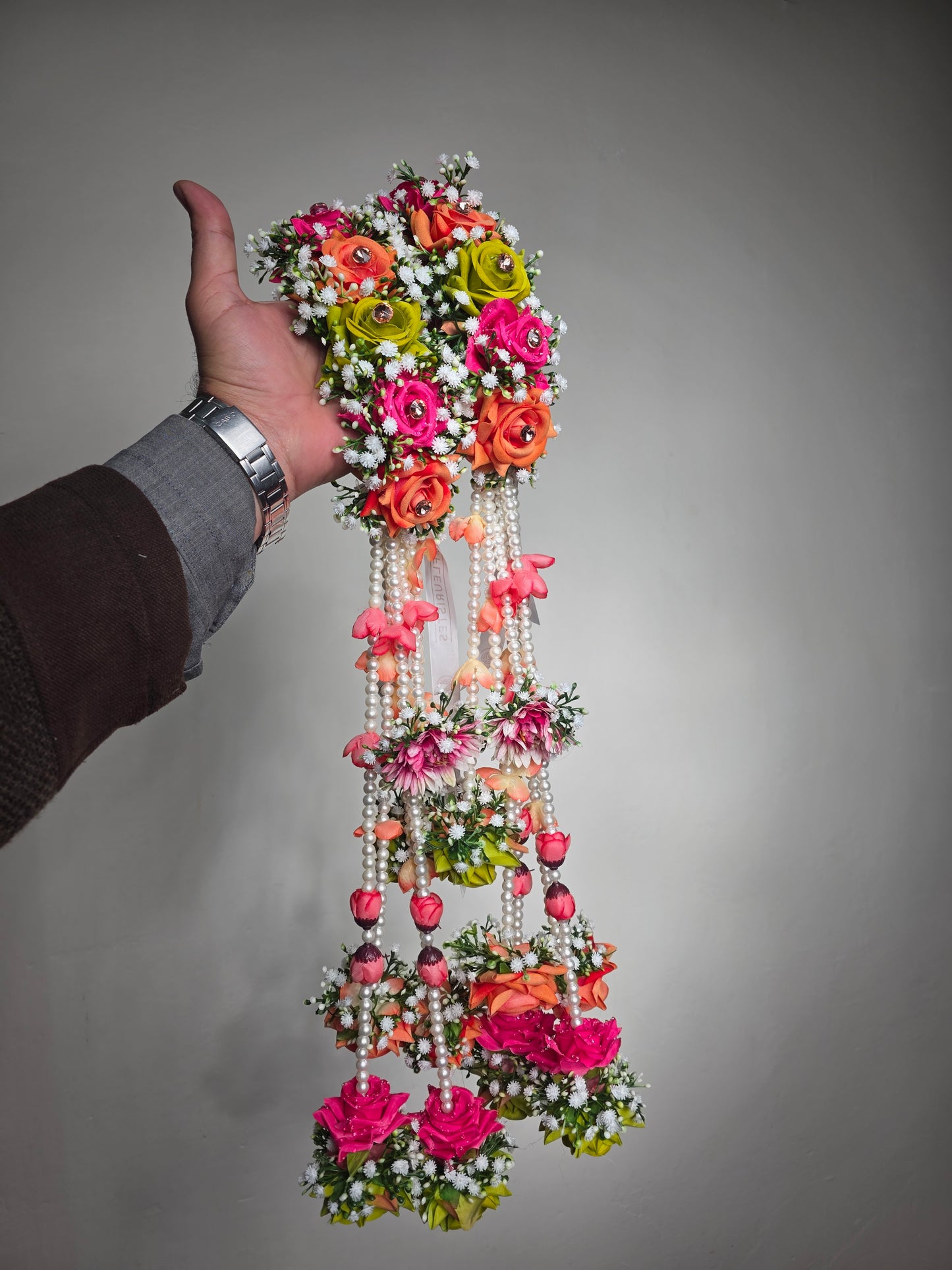 Decorative headband with flowers and pearls held by a person against a gray background