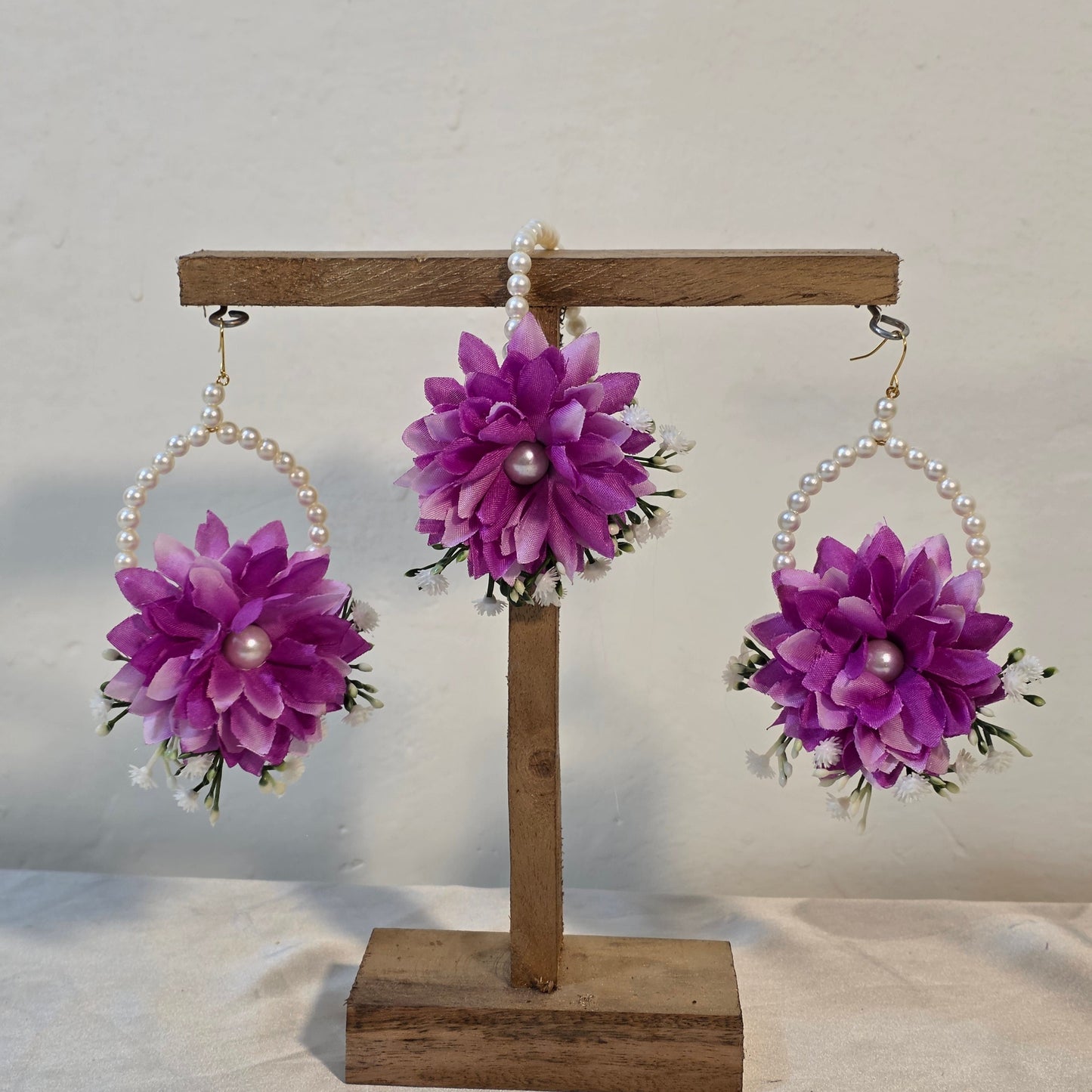 Three purple floral hair accessories with pearl centers on a wooden stand against a white background.