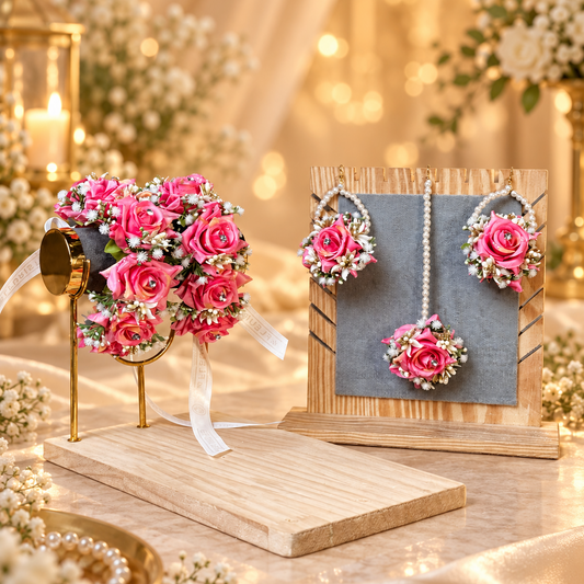 Pink floral jewelry and matching floral accessories displayed on stands in a warm, softly lit setting with candles and blurred lights in the background.