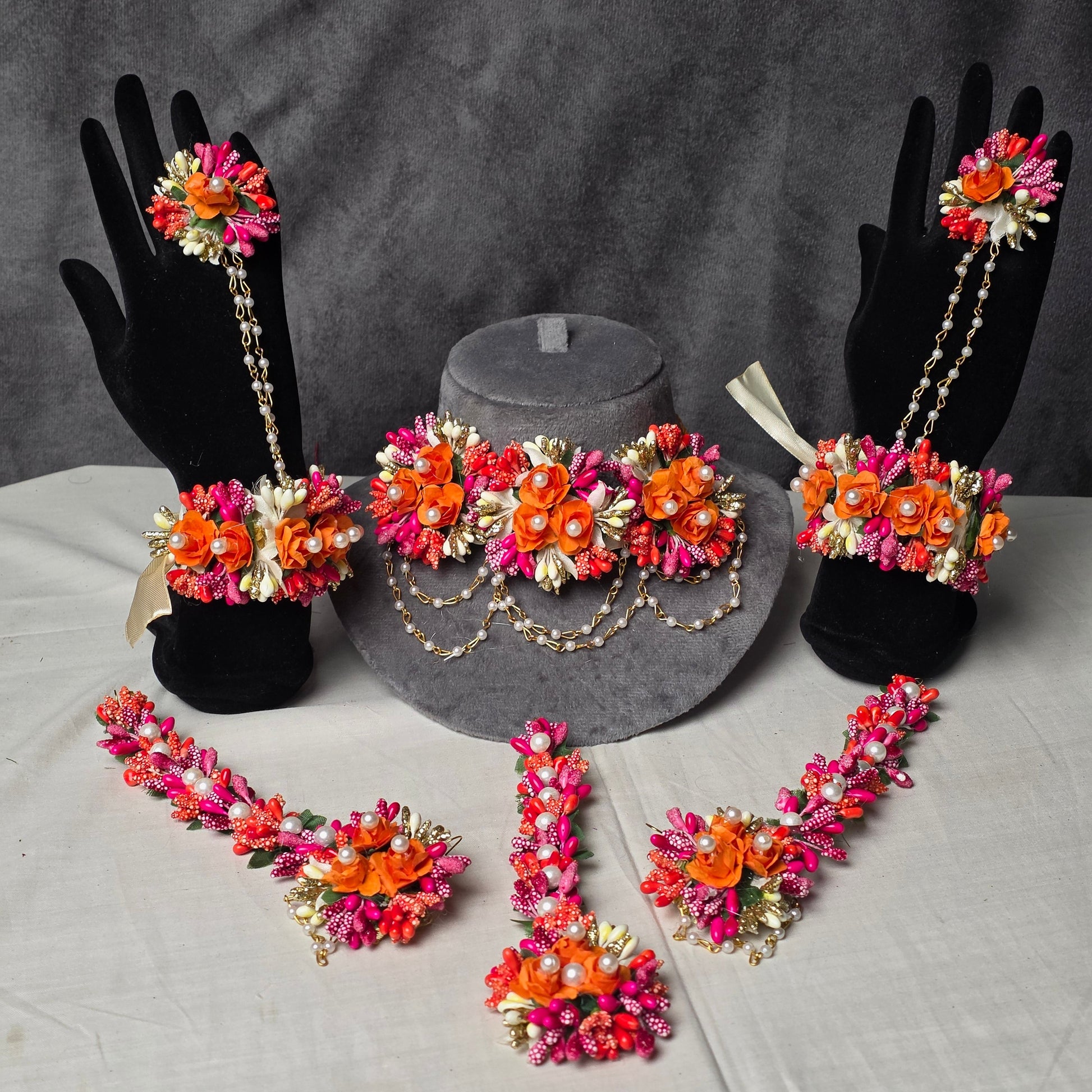Complete artificial floral jewelry set in vibrant orange and shocking pink for Pakistani Mehndi brides, featuring gajray, earrings with saharay, bindi, and necklace by De Fleuristes.