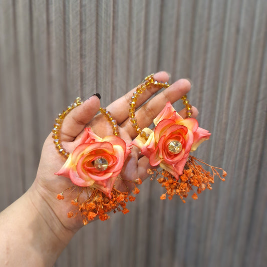 Hand holding a decorative hair clip with orange flowers and beads against a neutral background