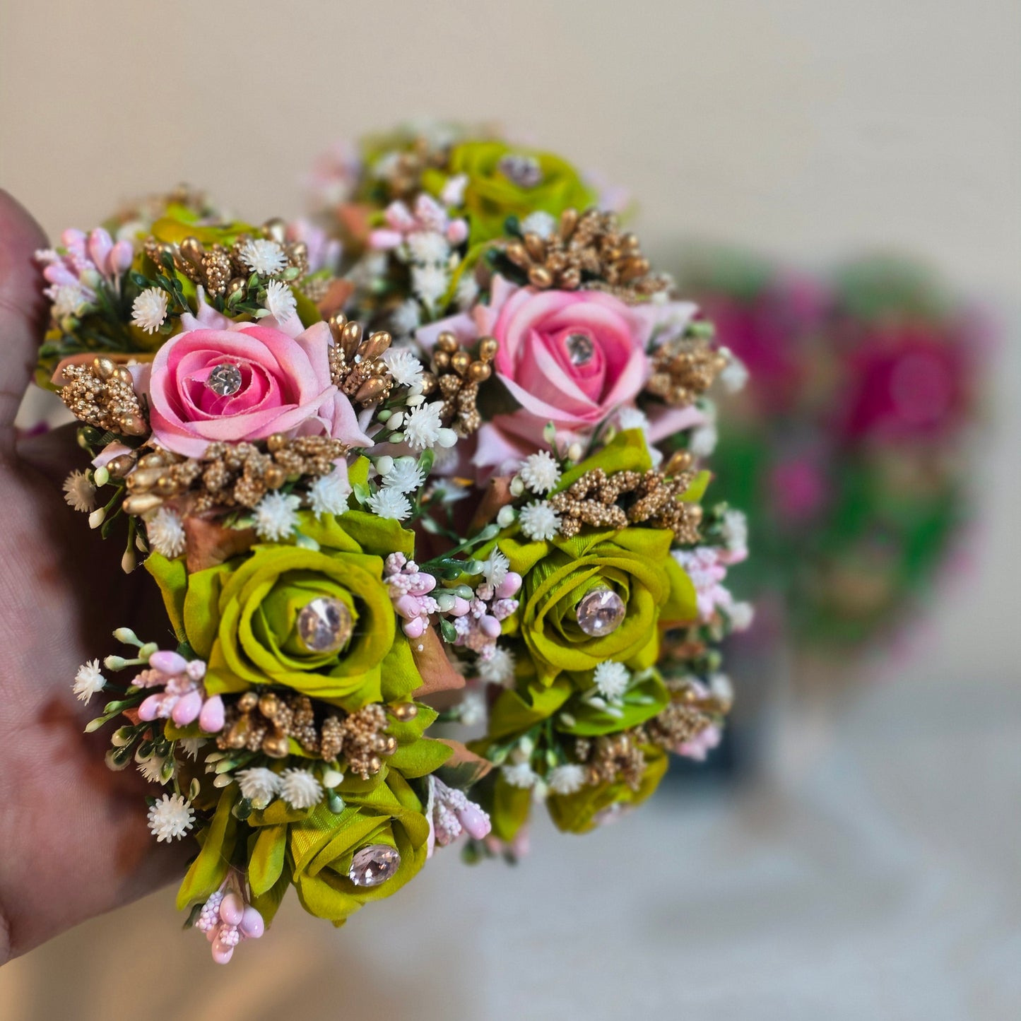 Hand holding a bouquet of artificial flowers with pink and green colors.