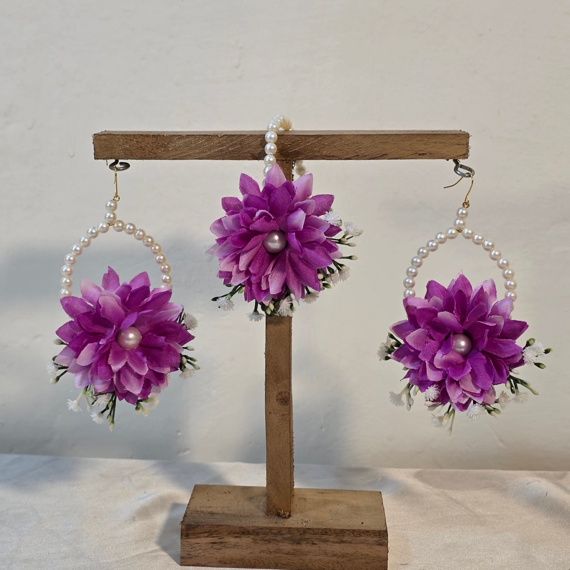 Three purple floral hair accessories with pearl centers on a wooden stand against a white background.