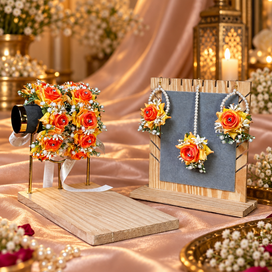 A styled jewelry display in a warm, bridal-themed setting. A wooden stand on the right holds a matching floral and pearl necklace, while another stand on the left holds a matching floral bouquet.